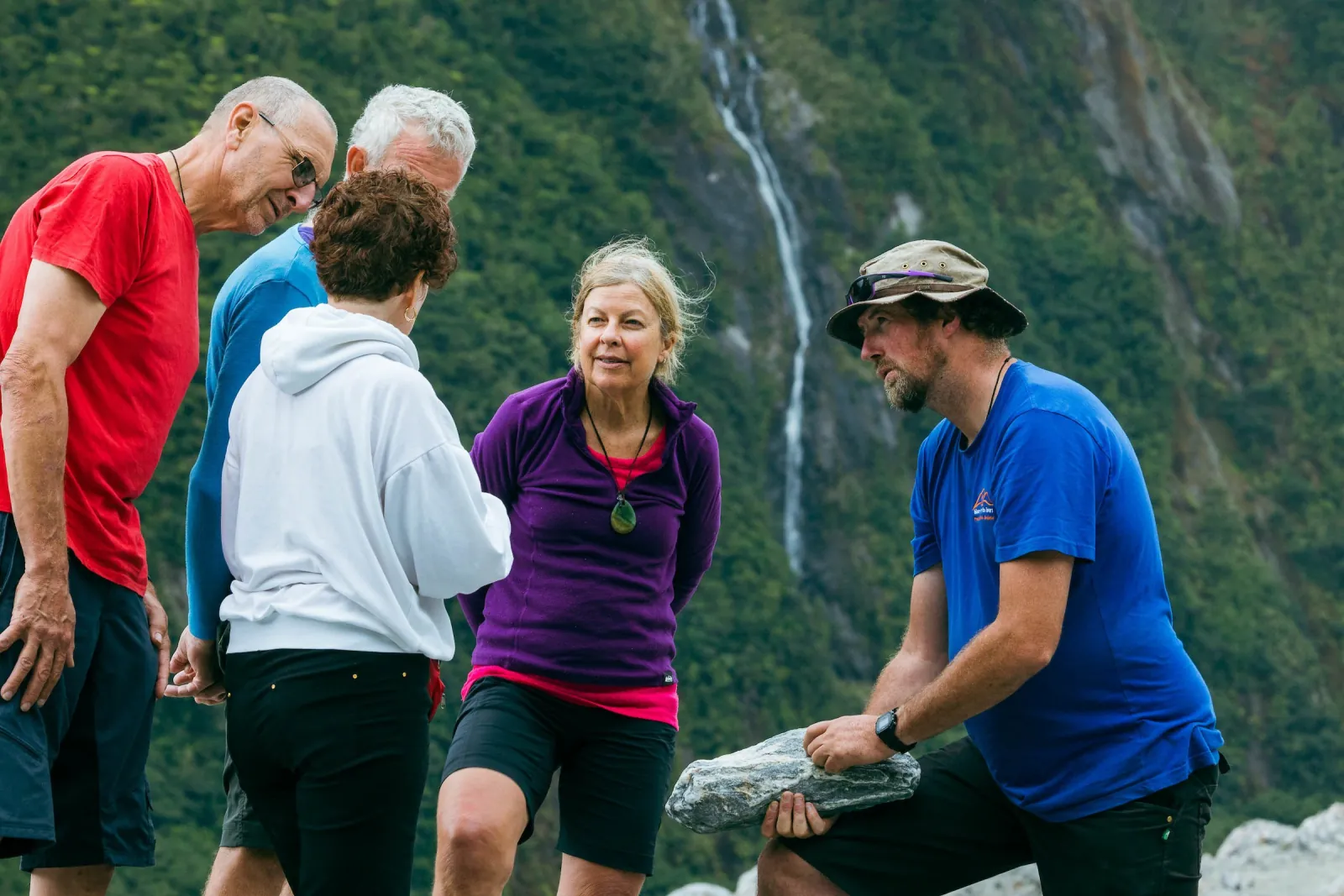 Guide showing a group a rock specimen with a waterfall on the cliff behind