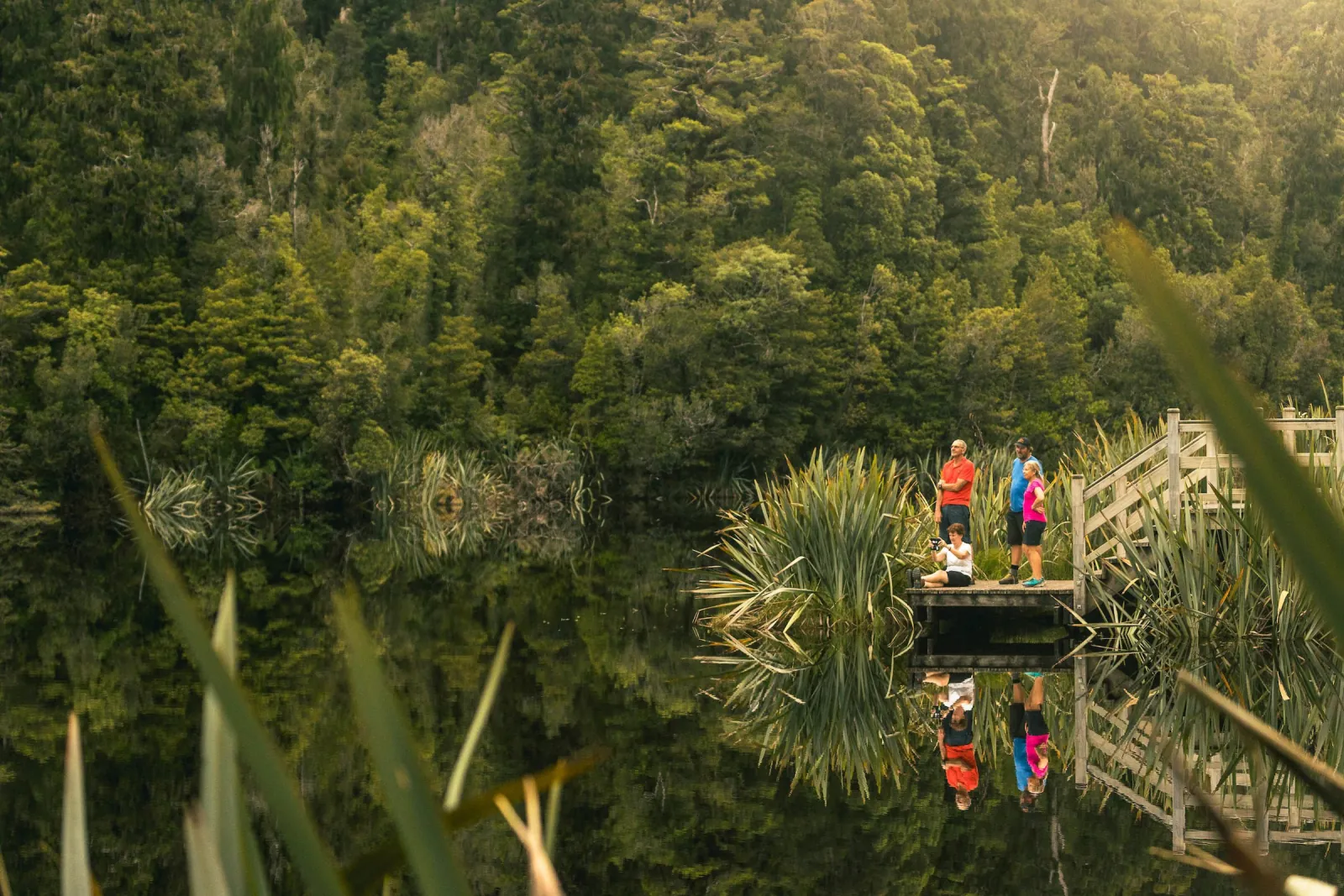 Two walkers on a wooden jetty at the forested edge of Lake Matheson